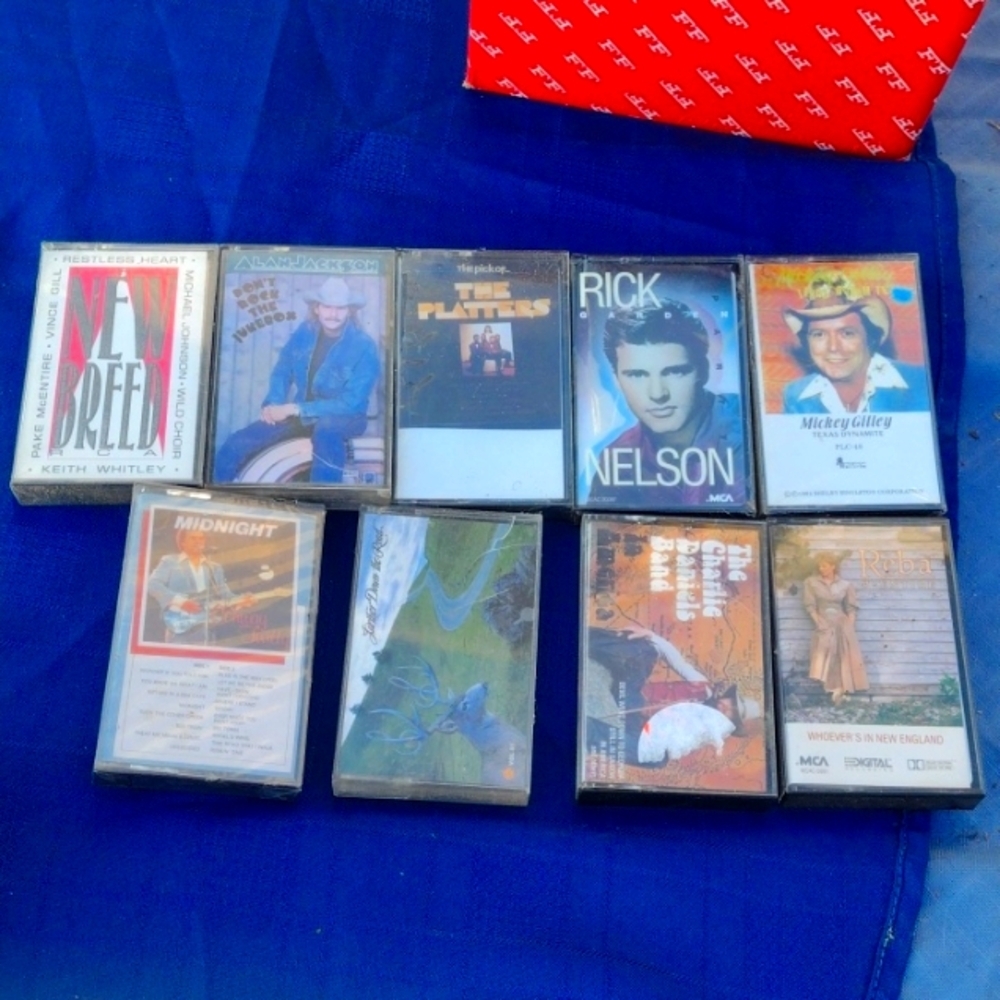 A spread of a dozen pre-recorded 1980s cassette albums laid out on a blue background, spines and cover art visible